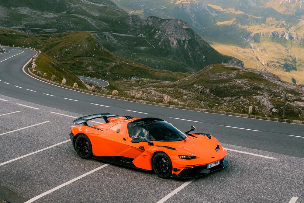 Oranje KTM X-Bow GT-XR op kronkelige bergweg met panoramisch uitzicht.