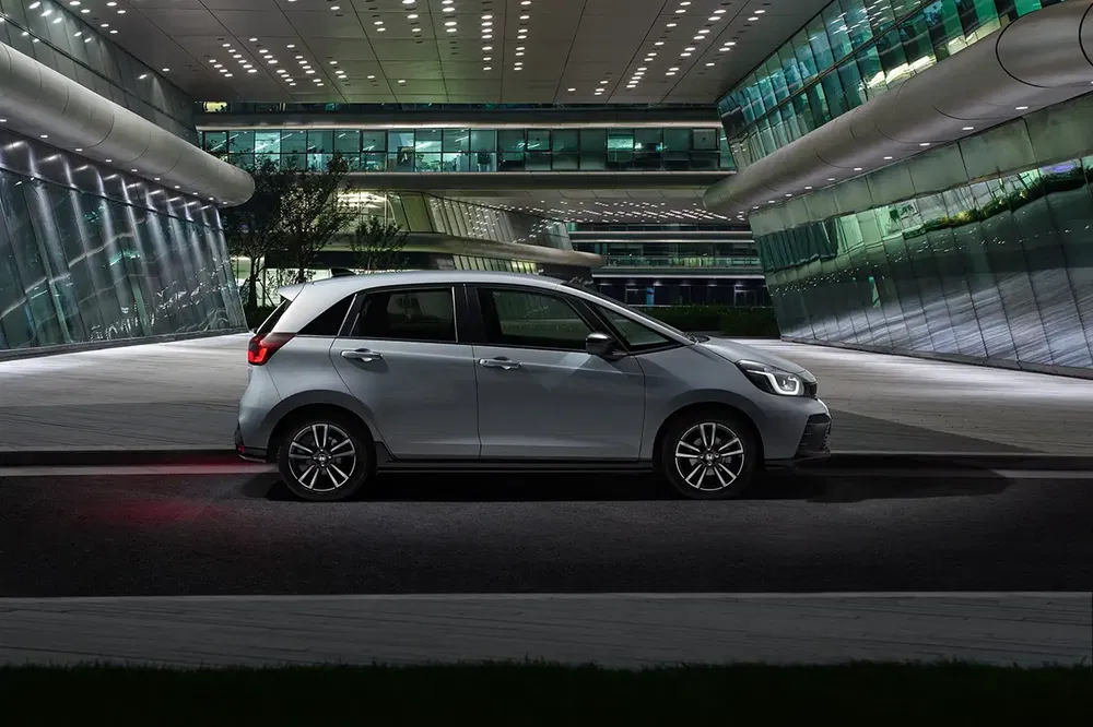 Moderne zilveren Honda Jazz voor futuristisch verlicht gebouw in de nacht.