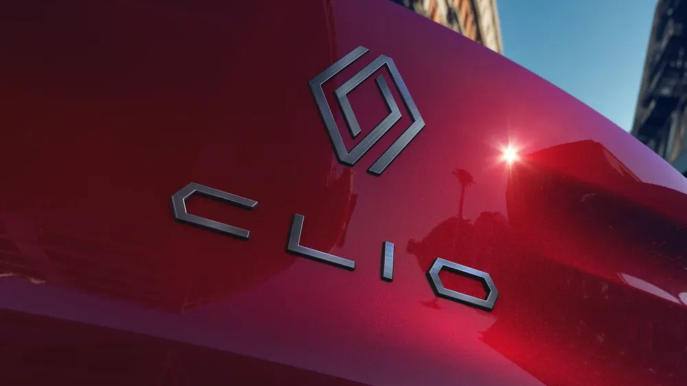 Renault Clio-embleem op glanzende rode carrosserie onder blauwe lucht.