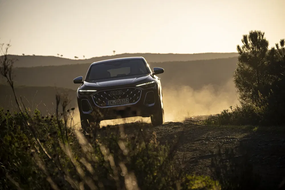 Audi Q5 roulant sur un chemin poussiéreux au coucher du soleil, lumière dorée du soir.