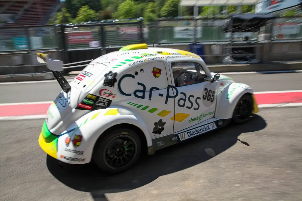 VW Beetle raceauto met Car-Pass livery op zonnig circuit.