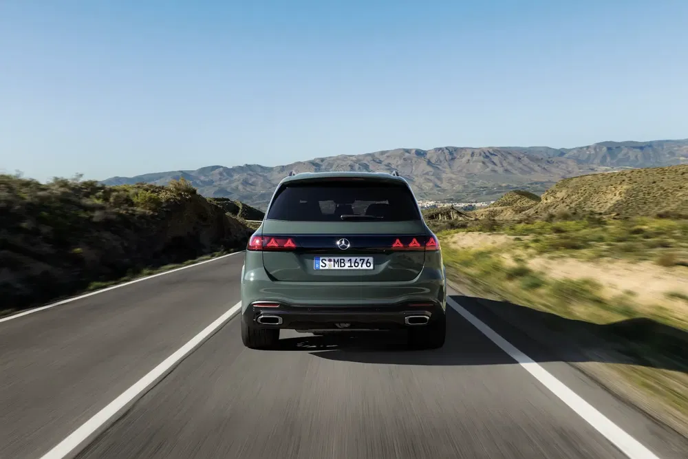 Mercedes-Benz SUV vert sur route de campagne, montagnes au loin sous ciel bleu clair.