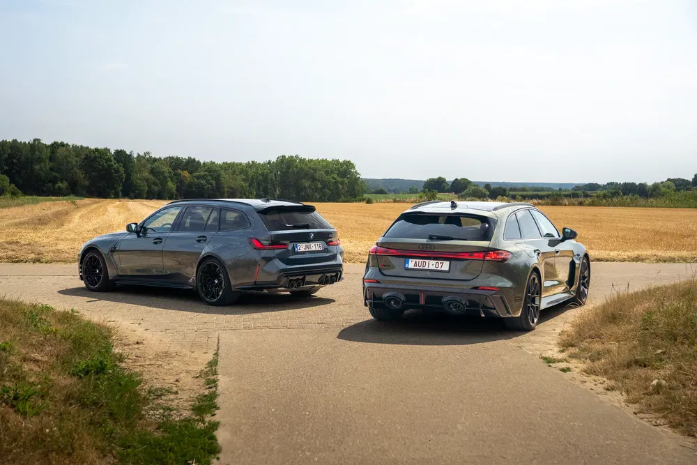 Twee sportieve stationwagens, BMW en Audi, op een landelijke weg.