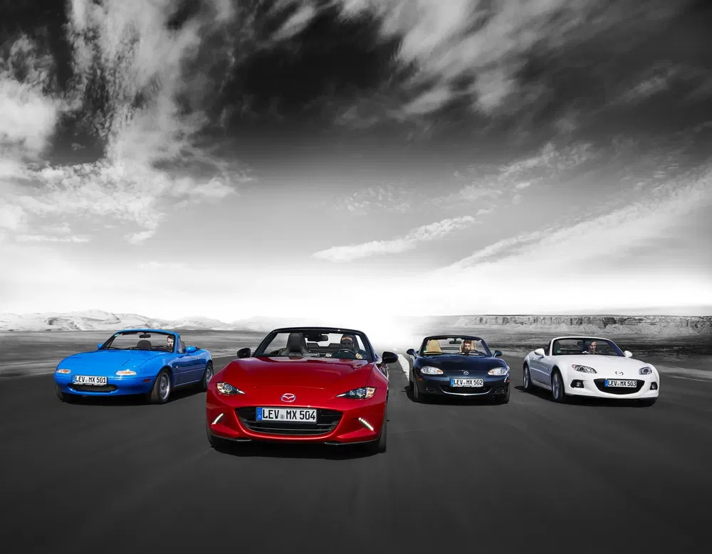 Gamme de Mazda MX-5 en conduite sur route déserte avec ciel dramatique en arrière-plan.