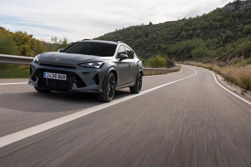 Cupra Formentor grise roulant sur une route sinueuse entourée de collines verdoyantes.