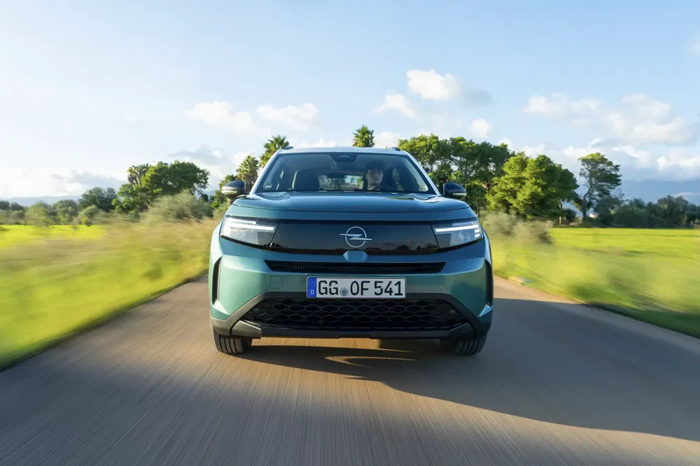 Opel Mokka vert roulant sur une route bordée d'arbres par temps ensoleillé.