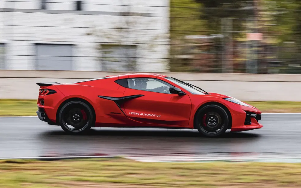 Rode Chevrolet Corvette rijdt op nat circuit, met gestroomlijnde moderne lijnen.