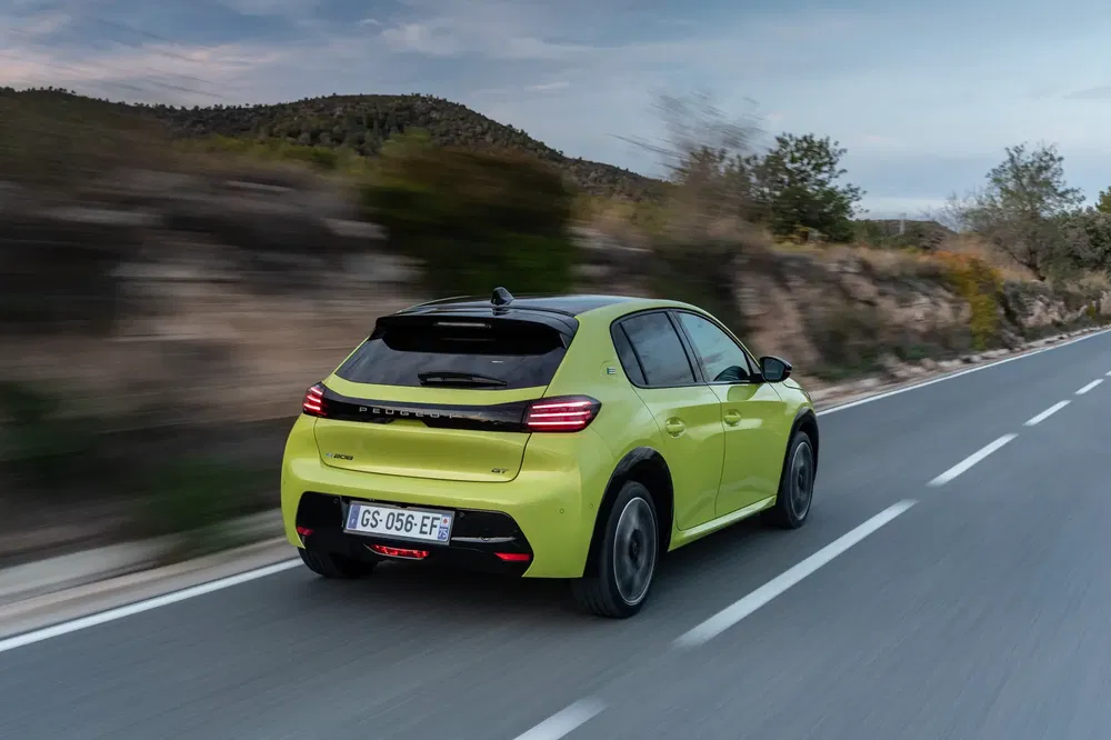 Peugeot 208 vert fluo roulant sur route de campagne au crépuscule.
