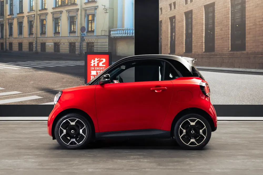 Rode Smart Fortwo geparkeerd binnen, met stadsreclame en gebouwen op de achtergrond.
