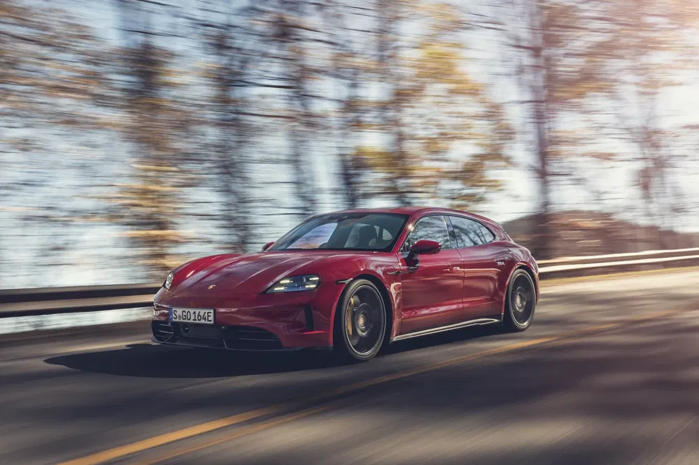 Porsche Taycan rouge roulant rapidement sur une route bordée d'arbres flous.