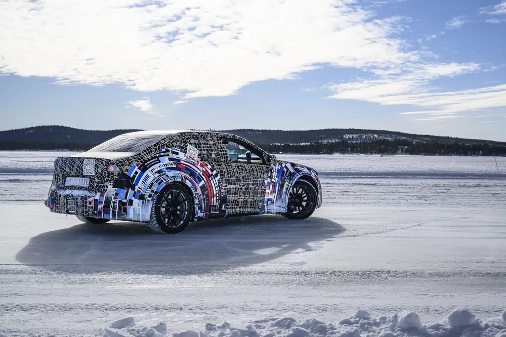 Camouflage auto prototype getest op een ijzige weg onder een bewolkte blauwe hemel.