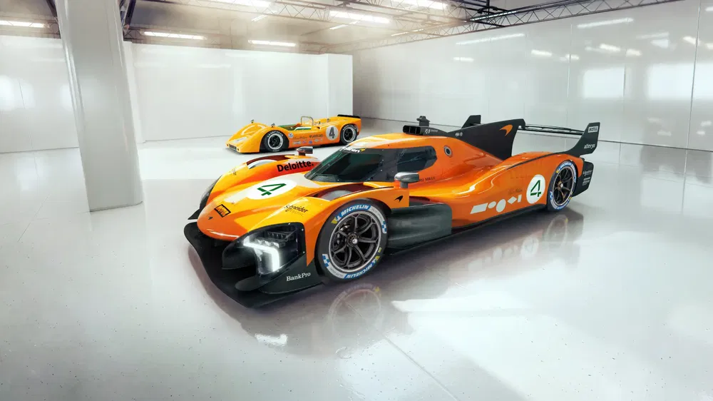 Voitures de course McLaren LMDh orange vif dans un garage moderne bien éclairé.
