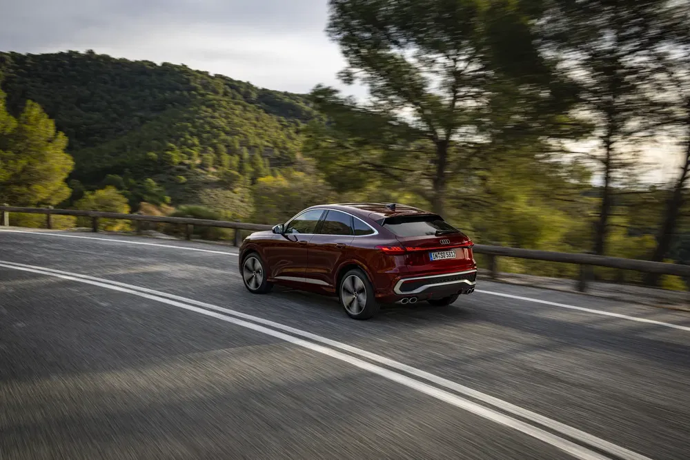 Audi Q5 Sportback rouge sur route sinueuse entourée de nature verdoyante.