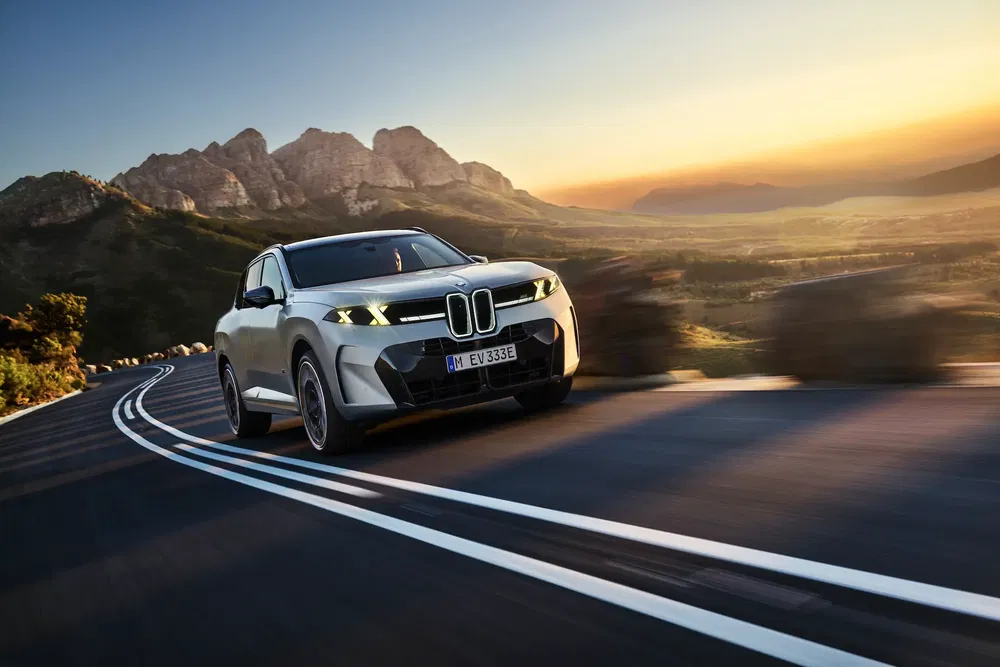 BMW iX3 roulant sur route sinueuse de montagne au coucher du soleil.