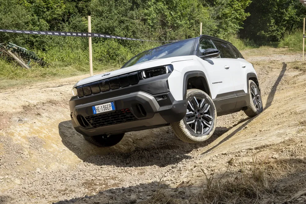 Jeep Compass blanc franchissant un terrain accidenté en plein air, démontrant sa capacité tout-terrain.