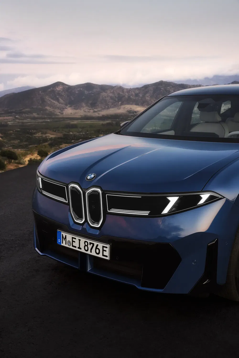Vooraanzicht van een BMW met kenmerkende grille tegenover bergachtig landschap.