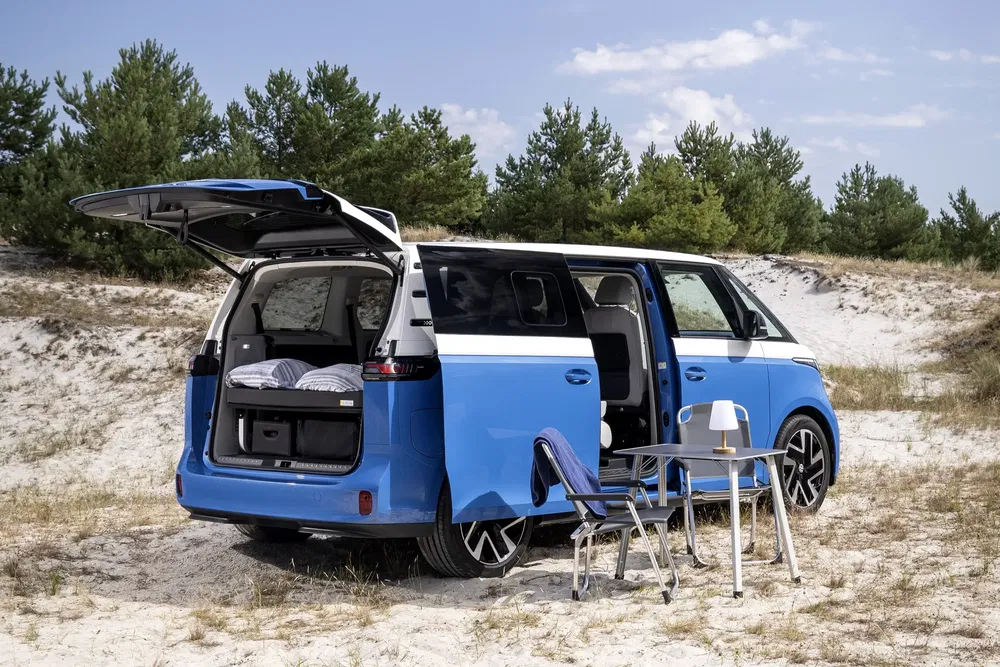 Volkswagen ID. Buzz en camping, tableau déplié, cadre naturel de dunes et pins.
