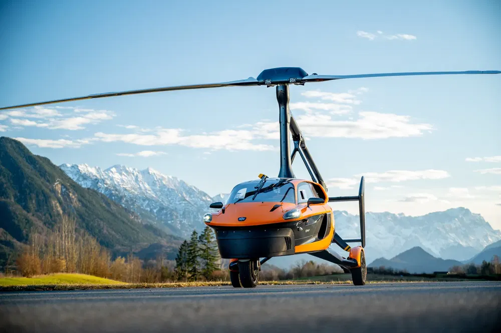 {"fr":"Voiture volante PAL-V Liberty orange sur piste, montagnes en arrière-plan.","nl":"Oranje PAL-V Liberty vliegende auto op de landingsbaan, bergen op de achtergrond."}