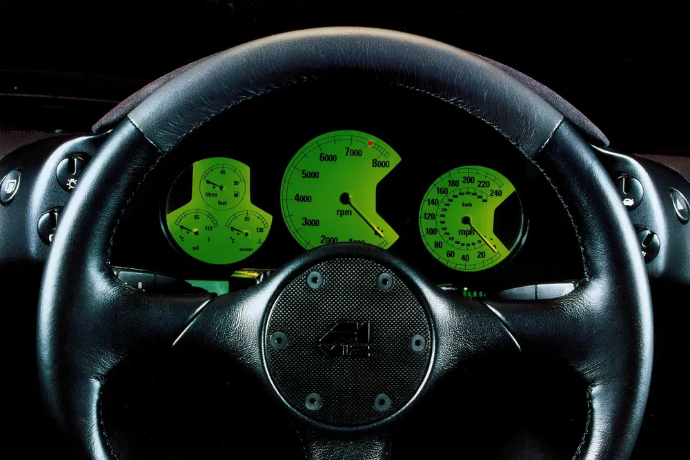 Tableau de bord rétroéclairé vert de l'Aston Martin DB7 affichant le tachymètre et le compteur kilométrique.