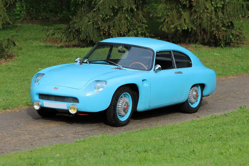 Voiture de collection DB HBR5 bleue, garée sur une route de campagne verdoyante.