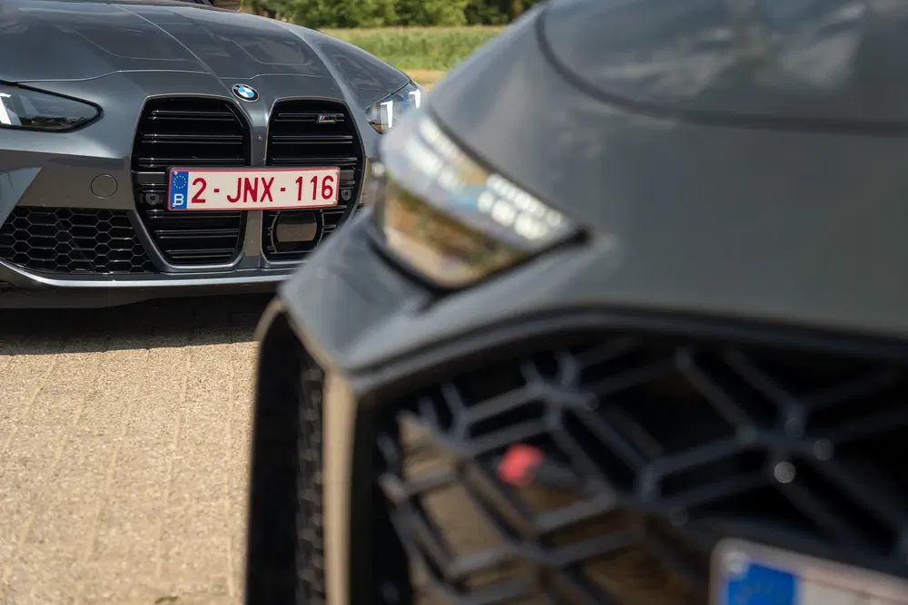 Twee sportwagens BMW M4 met Belgische nummerplaten op een zonnige weg.