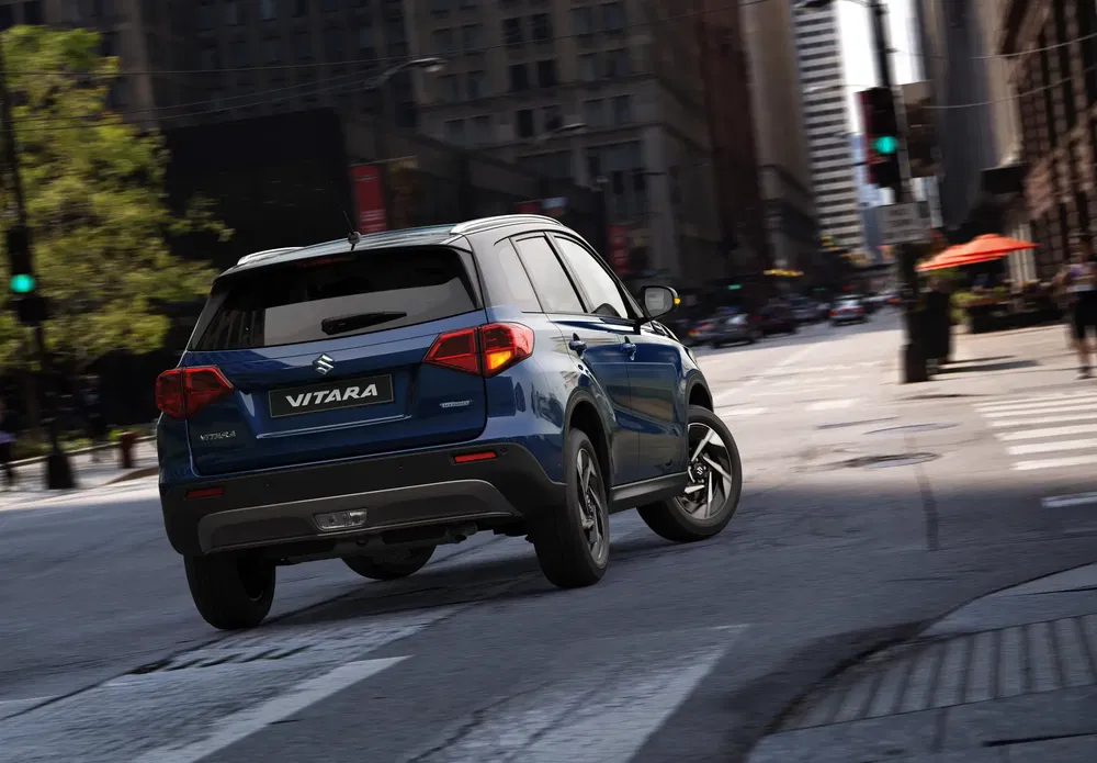 Suzuki Vitara bleu en ville, SUV traversant une intersection urbaine en journée.