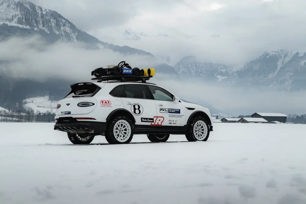 Witte Bentley Bentayga op sneeuw, uitgerust voor avontuur met bergen op de achtergrond.