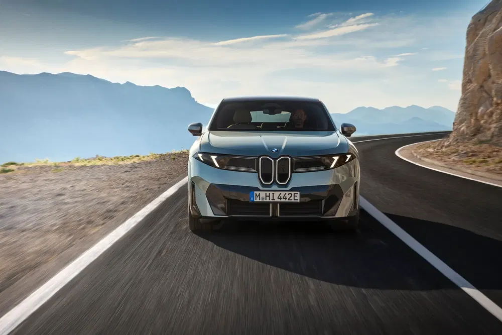 BMW i5 électrique roulant sur une route de montagne sinueuse par temps ensoleillé.