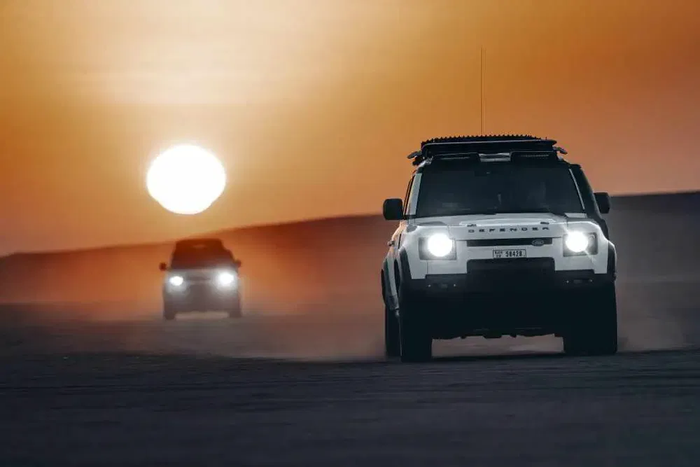 Deux Land Rover Defenders traversant le désert au coucher du soleil.
