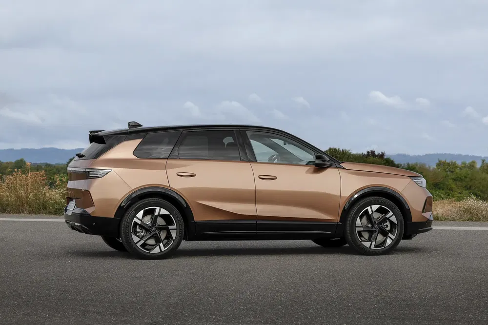 Vue latérale du SUV Opel Grandland 2024, couleur bronze, sur une route panoramique.