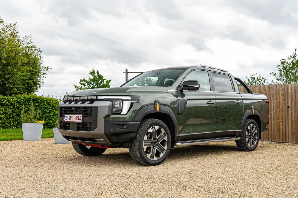 Pick-up électrique vert foncé sur allée gravillonnée avec ciel nuageux.