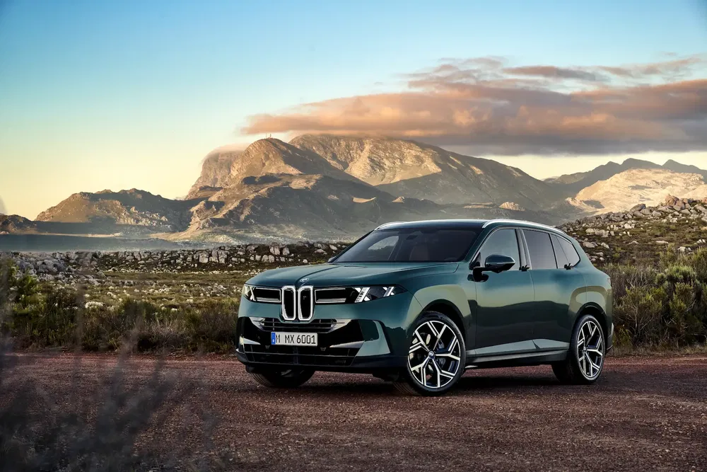 SUV BMW X5 vert sur une route montagneuse au coucher du soleil.