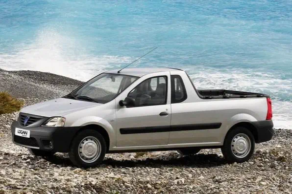 Pick-up Dacia Logan argenté sur une plage rocheuse avec la mer en arrière-plan.