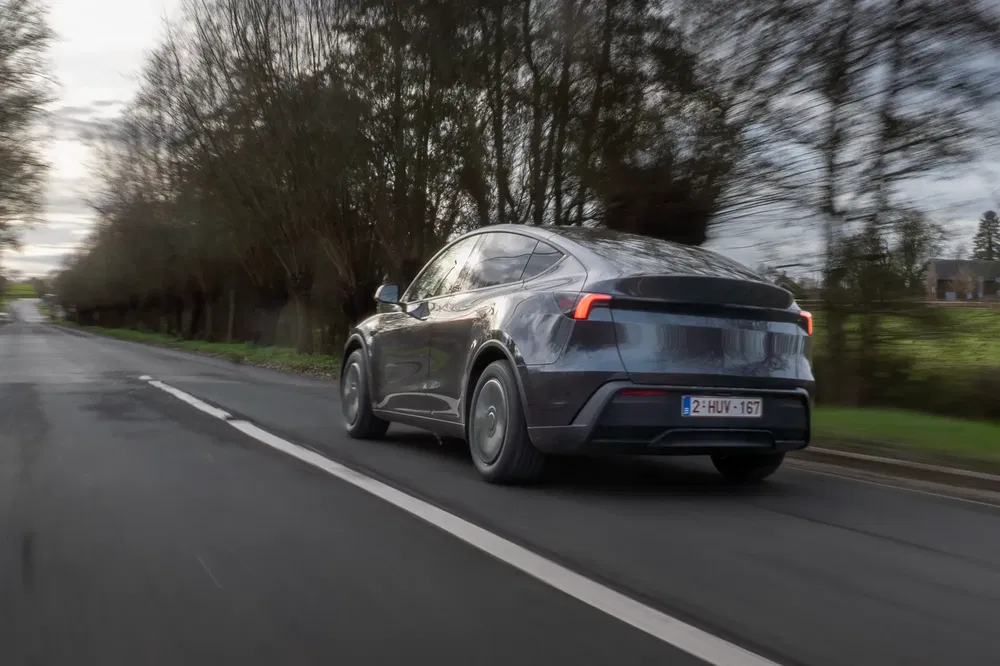 Tesla Model Y rijdt op een landelijke weg, bomen op de achtergrond.