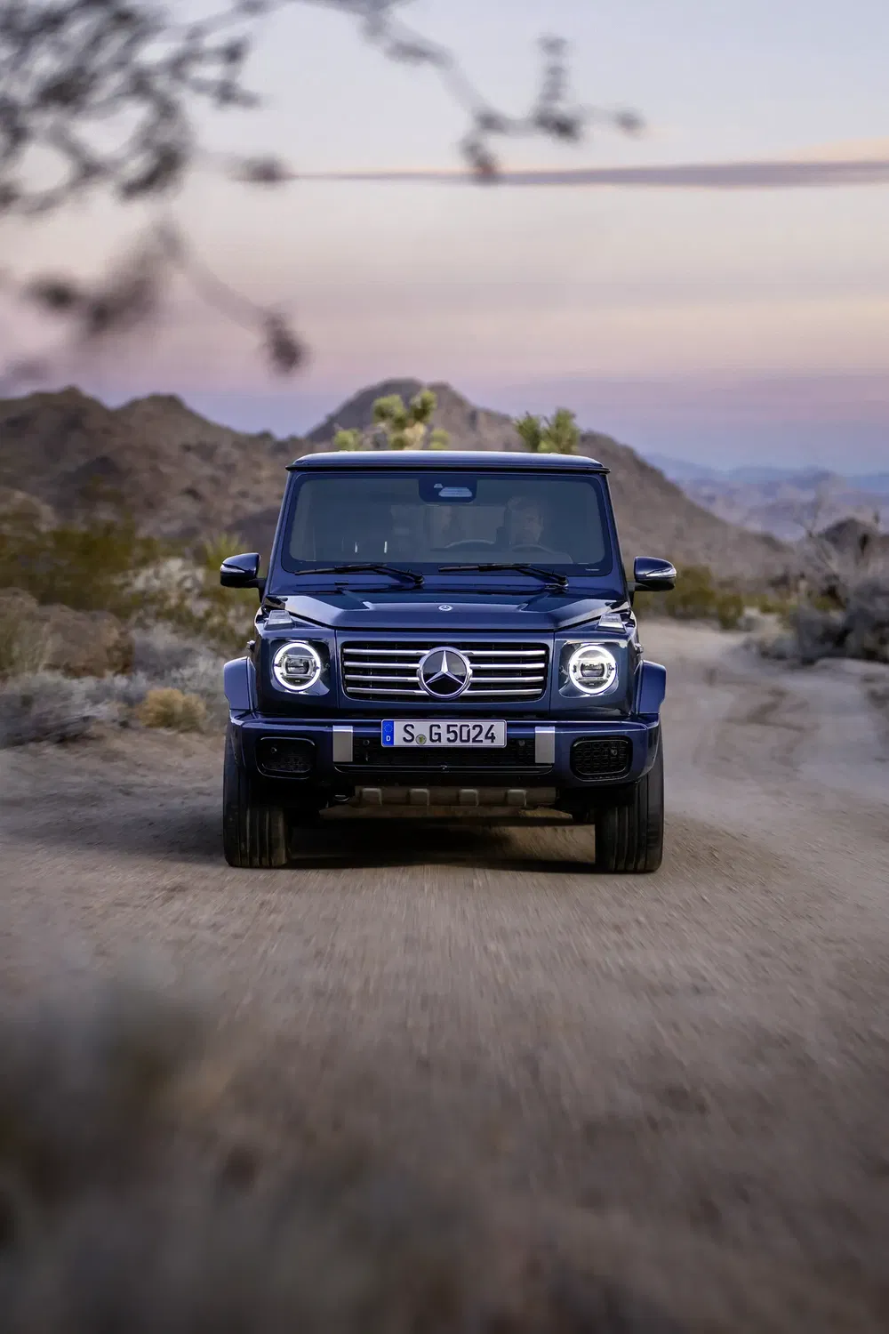 Mercedes G-Klasse rijdt op zandweg bij zonsondergang in een woestijnlandschap.