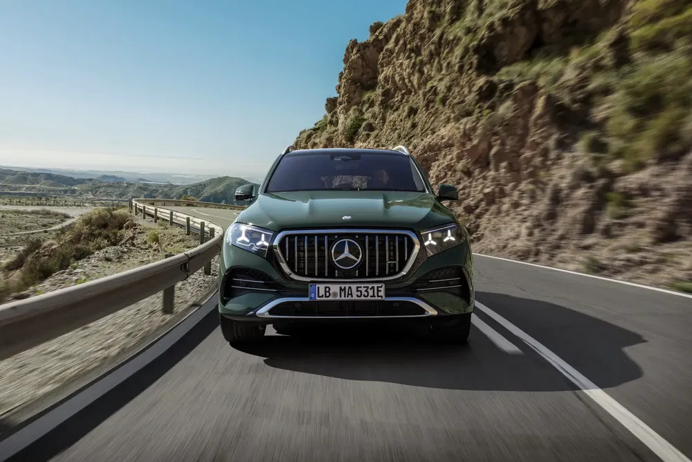 Groene Mercedes-Benz GLS rijdt op bochtige bergweg bij zonnig weer.