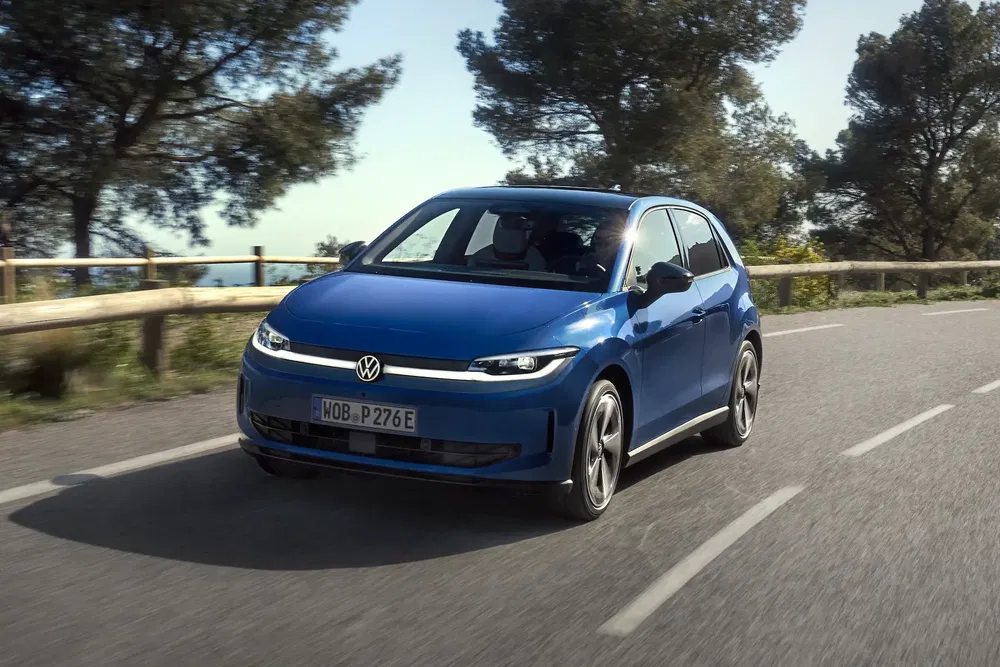 Blauwe Volkswagen Golf rijdt op een met bomen omzoomde weg op een zonnige dag.