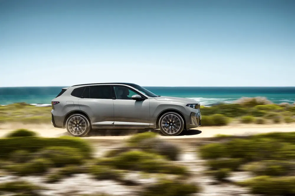 BMW X5 roulant le long d'une route côtière panoramique avec la mer en arrière-plan.