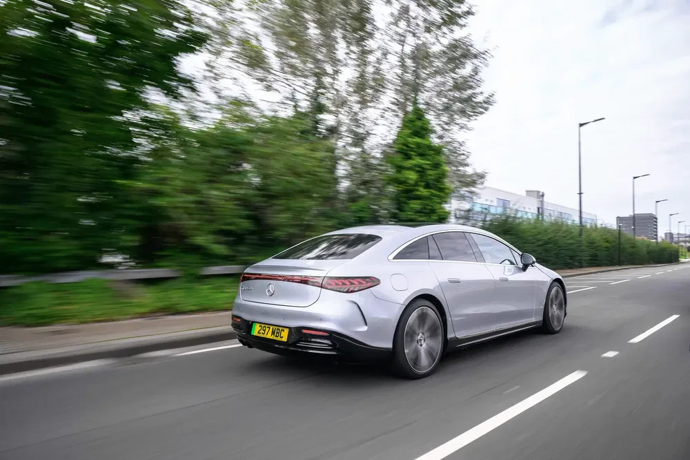 Mercedes-Benz EQS argent roulant sur une route bordée d'arbres en pleine journée.