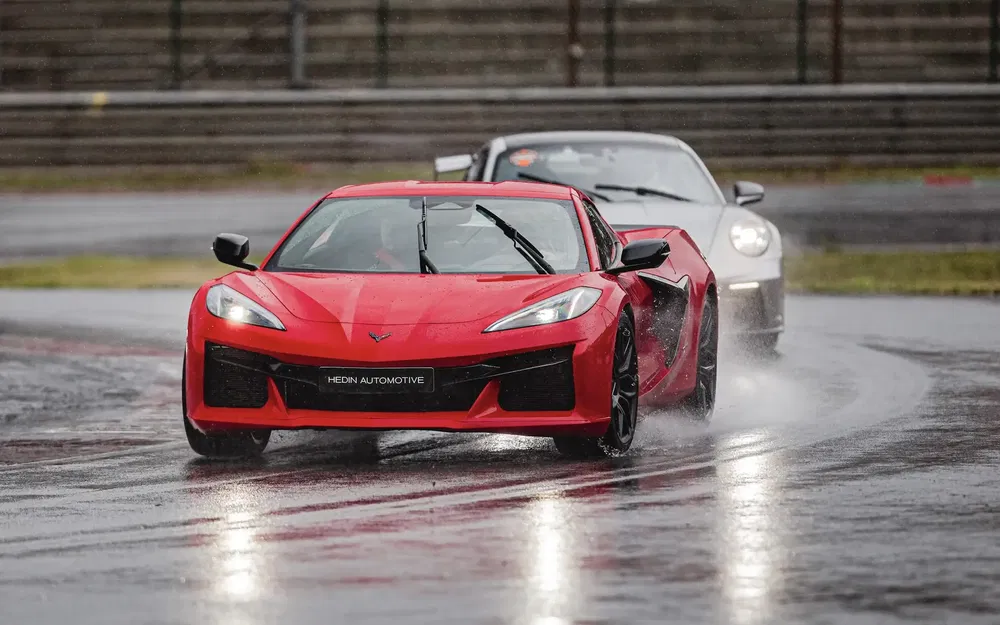 Rode Corvette en grijze Porsche op nat circuit tijdens race.
