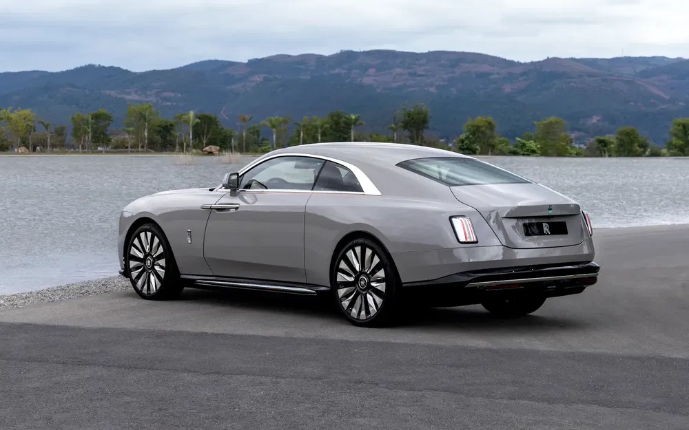 Voiture de luxe Rolls-Royce grise garée près d'un lac, montagnes en arrière-plan.