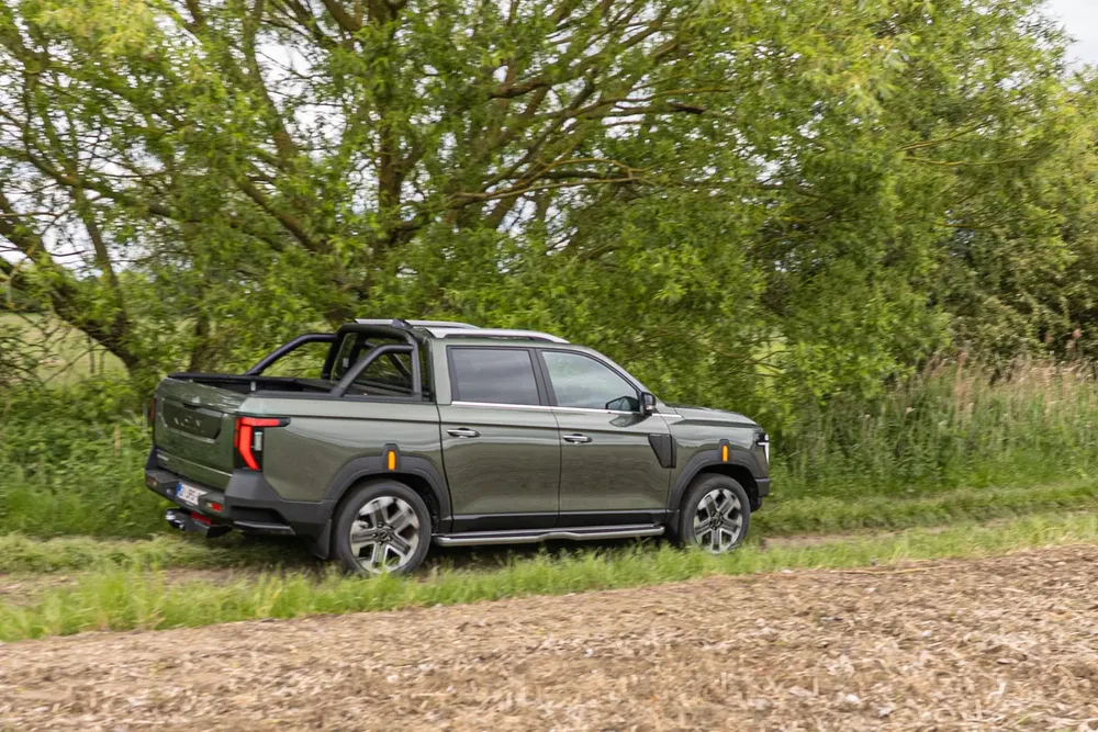 Pick-up Maxus T90 vert, roulant sur un chemin de terre près d'arbres verdoyants.