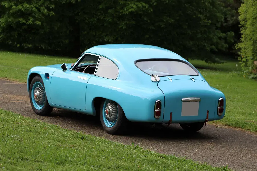 Voiture classique bleu clair stationnée dans un parc verdoyant en arrière-plan.