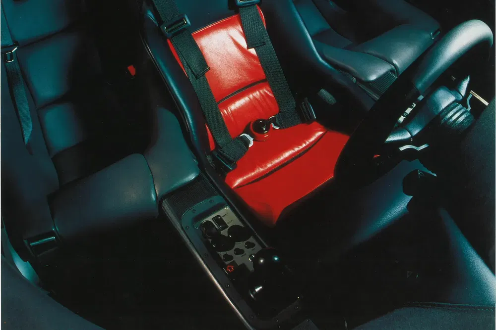 Intérieur voiture avec siège rouge en cuir et harnais de sécurité dans une ambiance sombre.