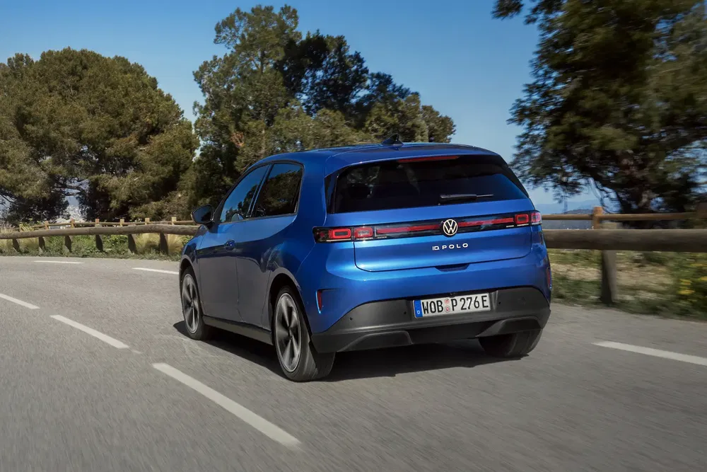 Blauwe Volkswagen ID.2 Polo op weg met bomen langs de kant, dynamische achteraanzicht.