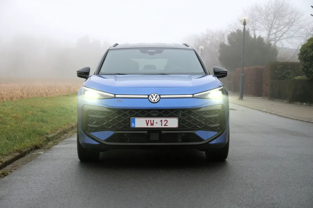 Blauwe Volkswagen T-Roc op mistige weg met Belgische kentekenplaat, lichten aan.