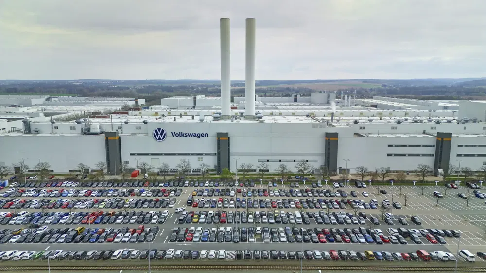 Usine Volkswagen avec parking rempli de voitures multicolores devant, ciel nuageux en arrière-plan.