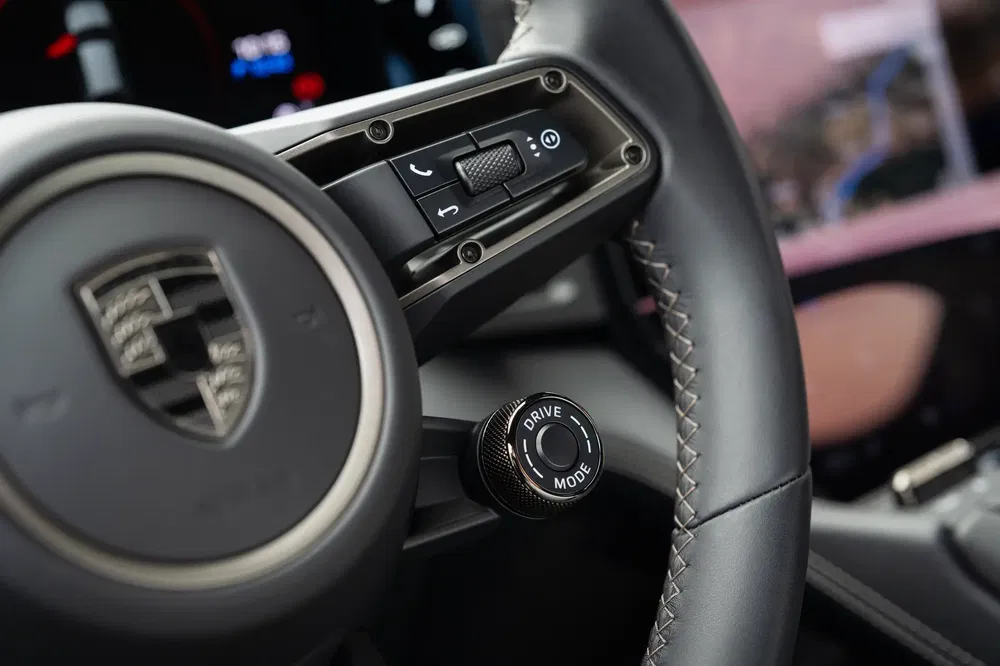 Volant Porsche avec bouton Drive Mode et commandes intégrées, détail intérieur sportif.