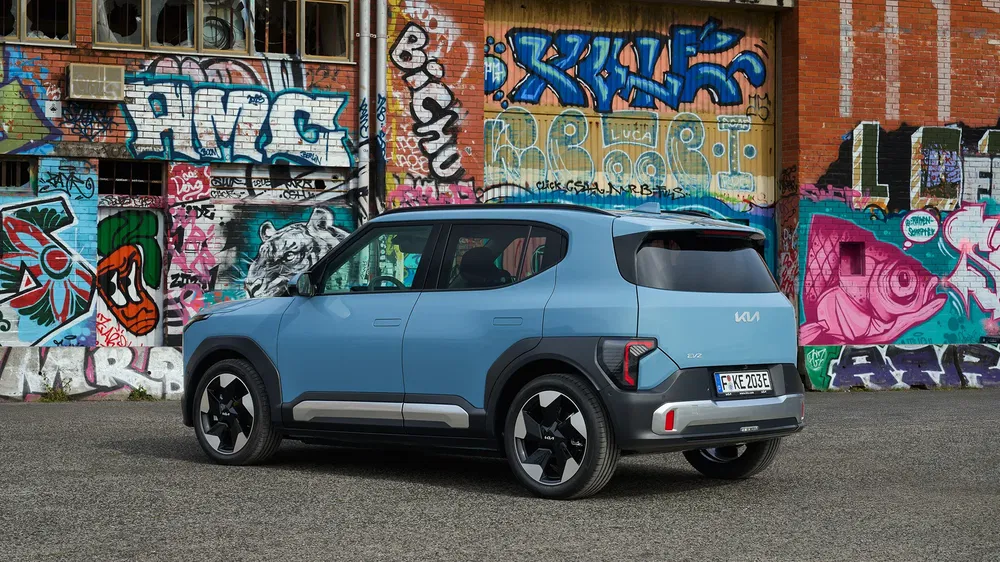 Kia SUV bleu devant un mur de graffitis colorés dans un quartier urbain.