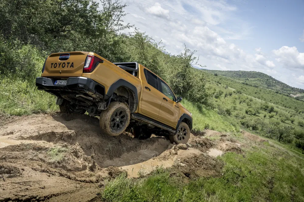 Toyota Hilux jaune franchissant un terrain boueux dans un paysage naturel.